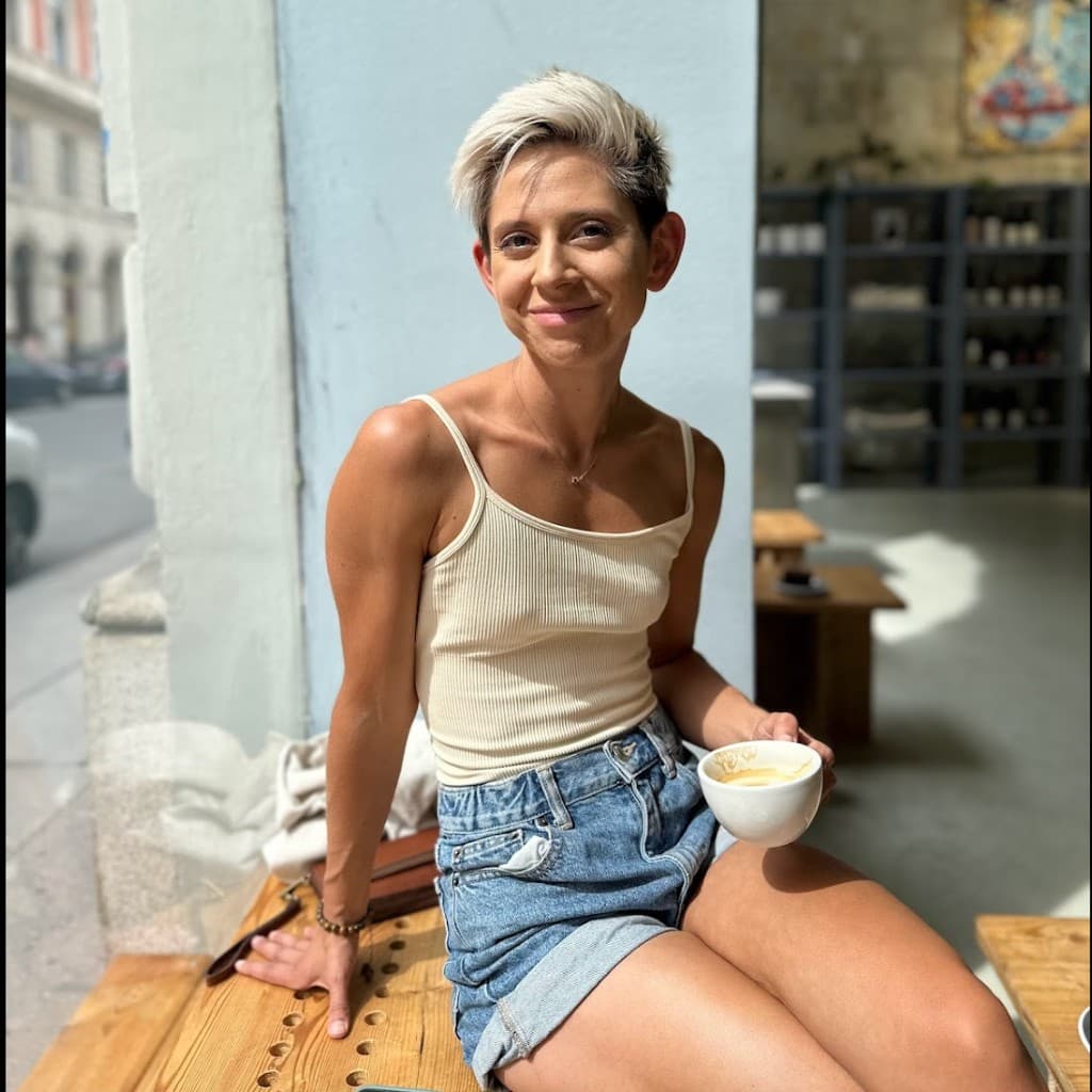 Portrait of Stacey Fronek sitting at an outdoor cafe holding a coffee cup, smiling at the camera
